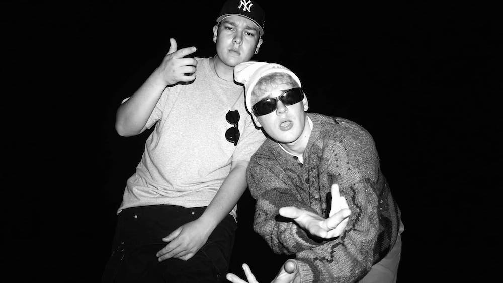 Black and white photo of Joey Valence and Brae, they pose for the camera, wearing sunglasses, and a New York Yankees hat. 