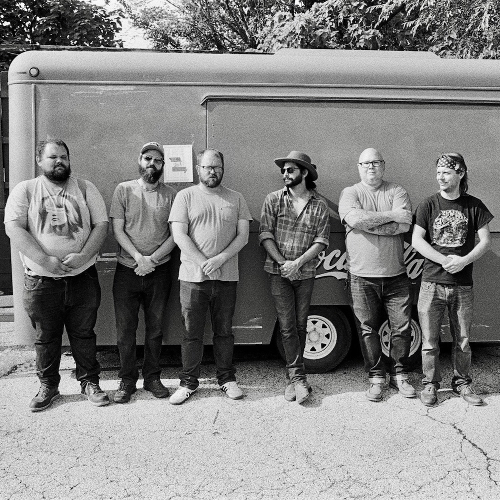 The members of Nick Gusman and the Coyotes stand outside in front of a trailer. The photo is in black and white.