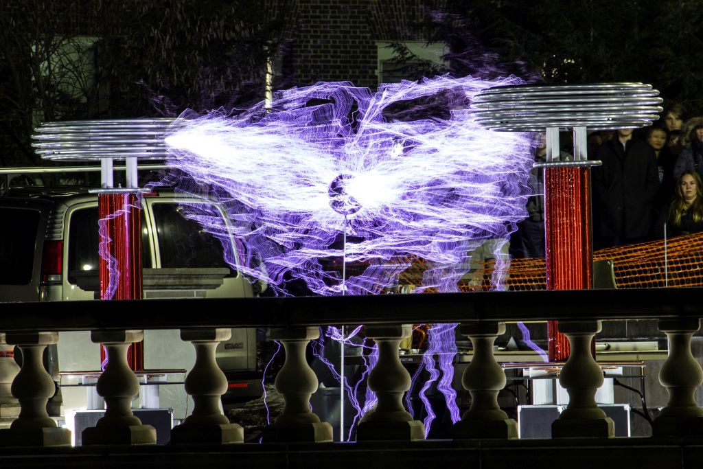 Two very large tesla coils with purple colored light reaching between them. 