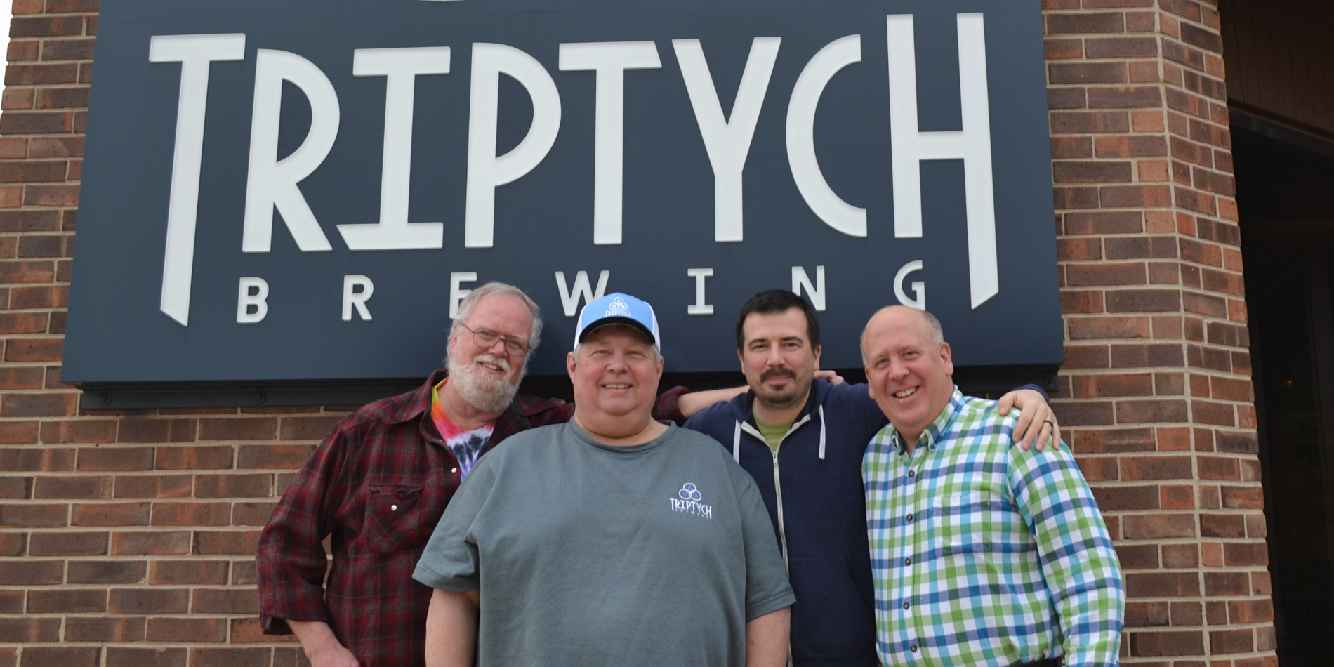 Four owners of Triptych Brewing stand in front of the navy sign outside the taproom in Savoy, Illinois.