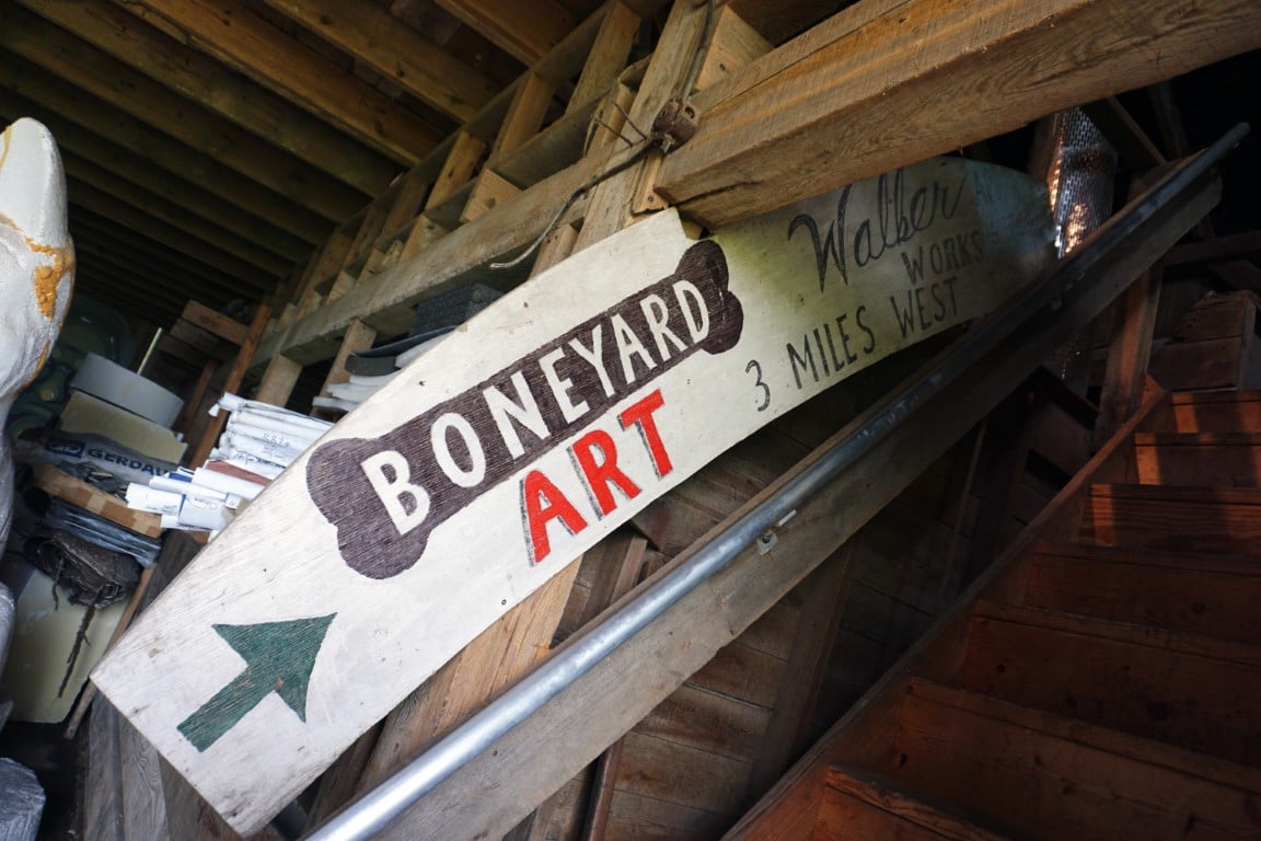 The inside of a dimly lit space. A wood sign is hand painted to say "boneyard festival" with an arrow pointing up a staircase