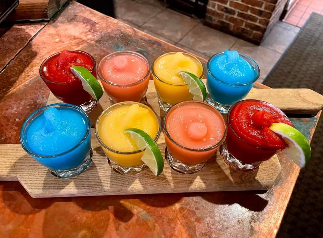 A tray of multi-colored frozen margaritas. Four are garnished with a lime wedge.