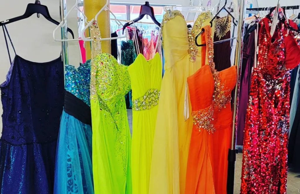 a clothing rack holds prom dresses in a rainbow of colors from dark blue to red.