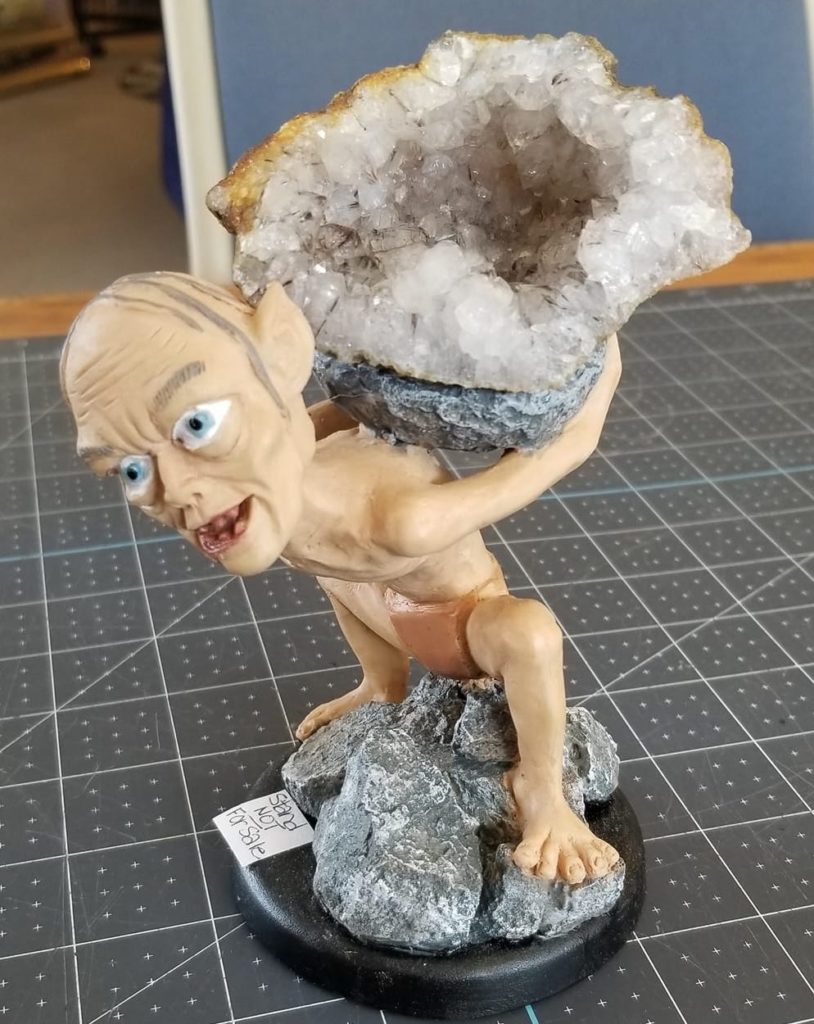 A white and gray gemstone is perched on a Lord of the Rings gollum stand. The stand is on a gray mat on a table. 