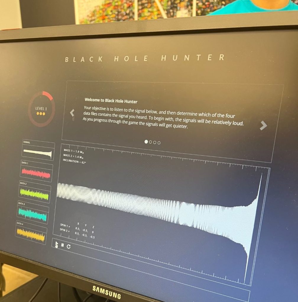 Close up of a monitor that says Black Hole Hunter at the top. It is displaying images of sound waves.