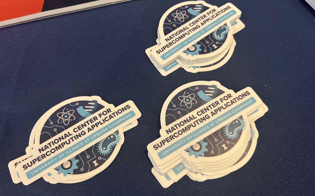A table with a blue covering has three stacks of stickers that say National Center for Supercomputing Applications.