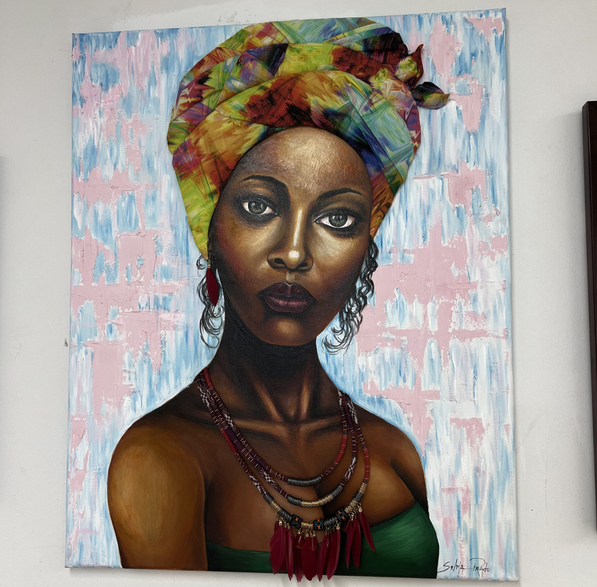 a painting of a black woman, wearing a colorful turban, with curly hair hanging out the back, a green strapless top, and a large necklace. 