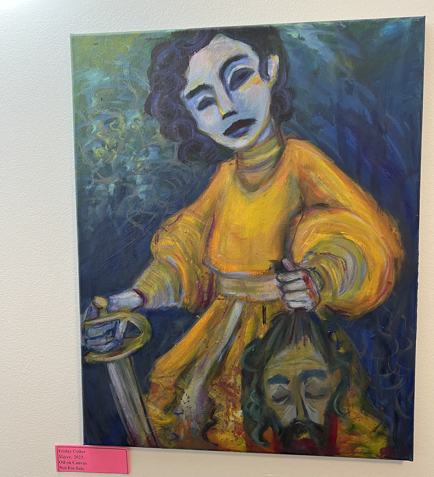 An oil on canvas painting "Slayer" depicts a young woman in a yellow dress holding a sword in her right hand an a decapitated male head in her right hand 
