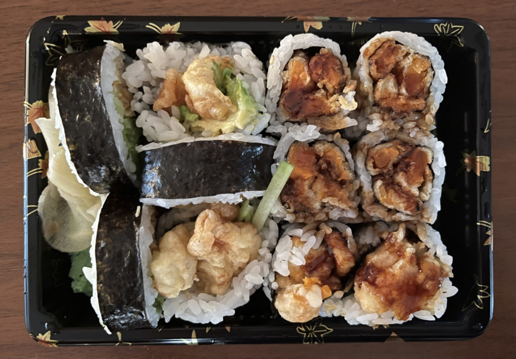 Chicken tempura and sweet potato tempura sushi in a black take out container. 