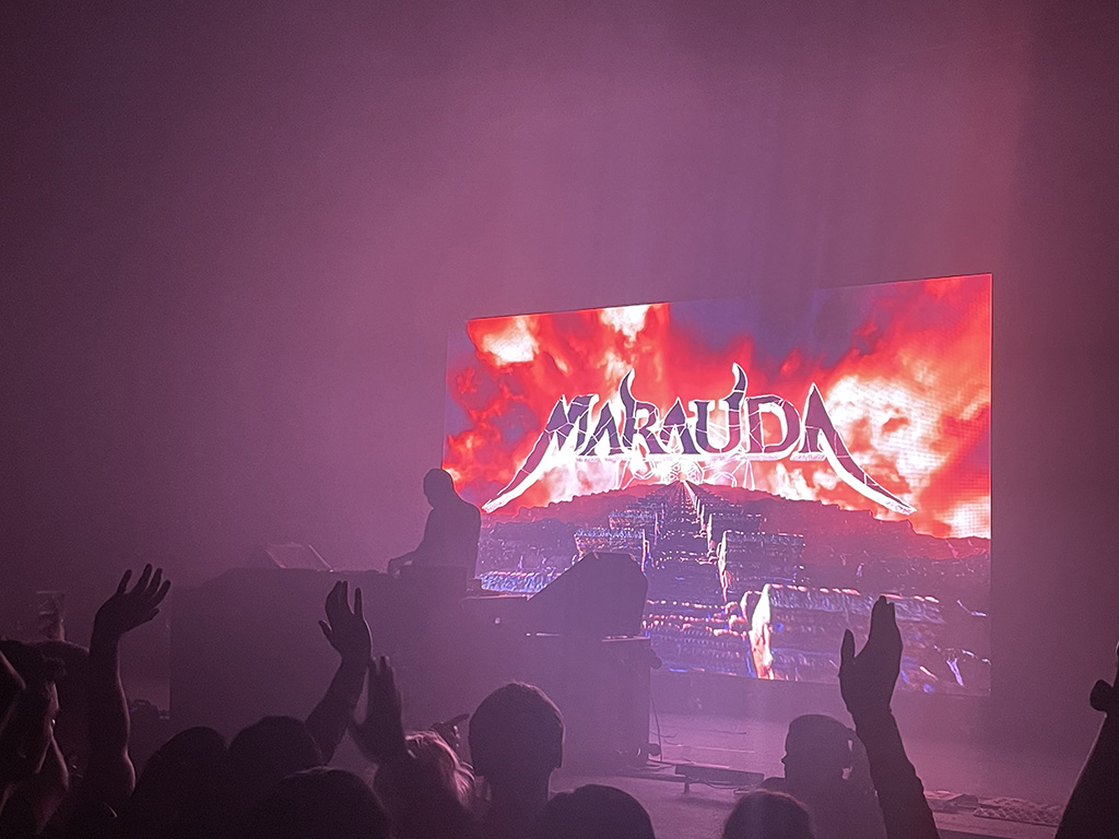 Shot of an EDM show at Canopy Club. You see several people in front of the stage, the artist Marauda mixing his music, and a video screen with "Marauda" on it behind him.