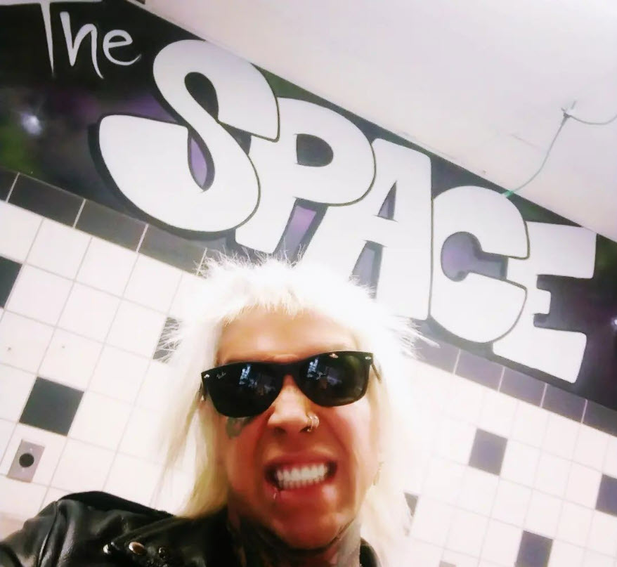 Lead Singer Austin Parker of Mid Nite Leg smiling below a mural on a wall that says "The Space".