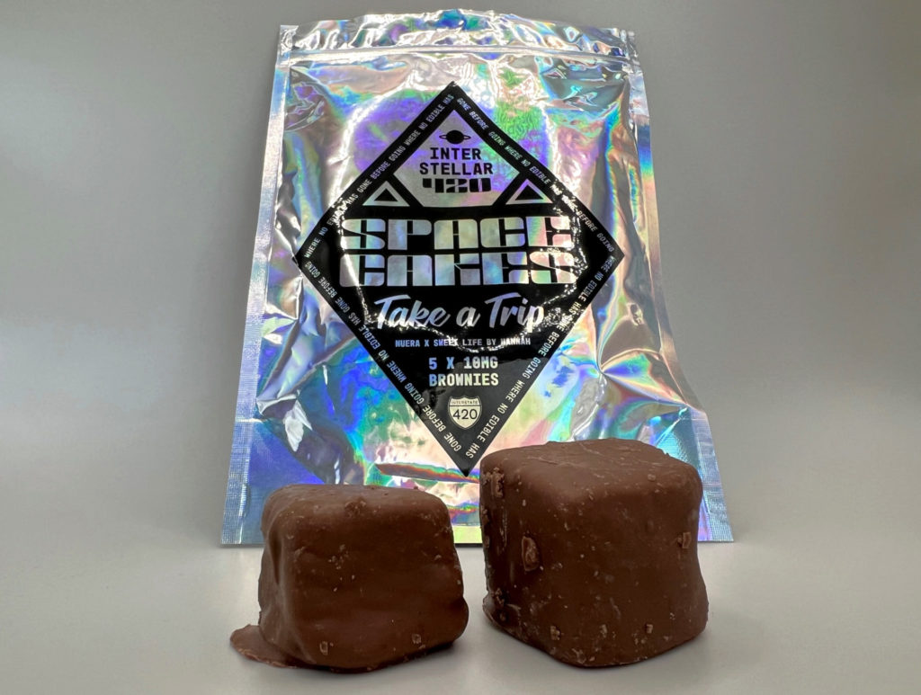 Space Cakes cannabis brownies are in front of a metallic, shiny bag reading Space Cakes in black ink from nuEra cannabis in collaboration with Sweet Life by Hannah for 4/20. Photo by Alyssa Buckley.