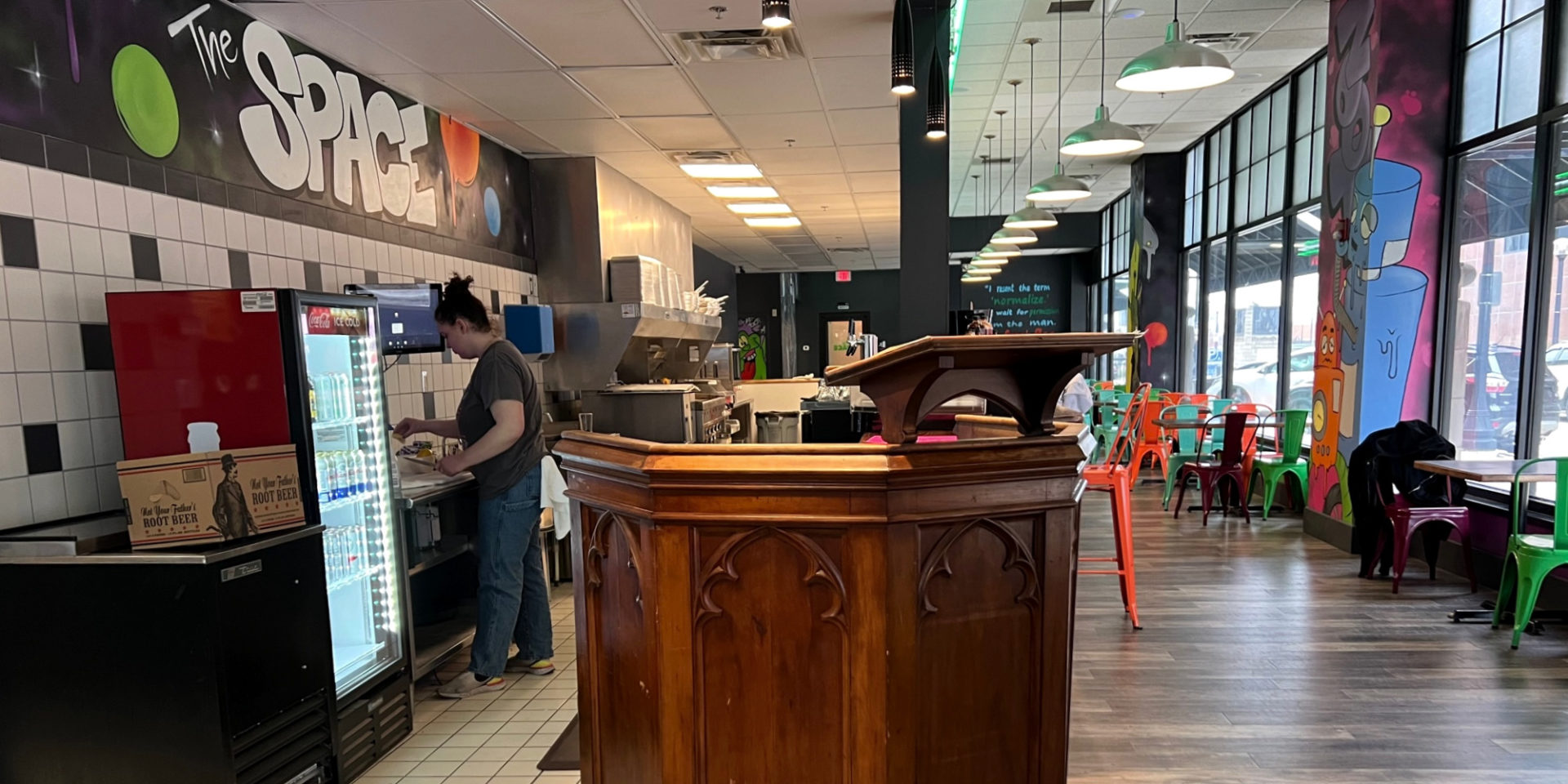 Inside The Space restaurant, new to Downtown Champaign. There is a wooden podium and a bar manager working at the counter. Chairs of bright orange and teal are tucked into brown tables and the bar. Photo by Alyssa Buckley.