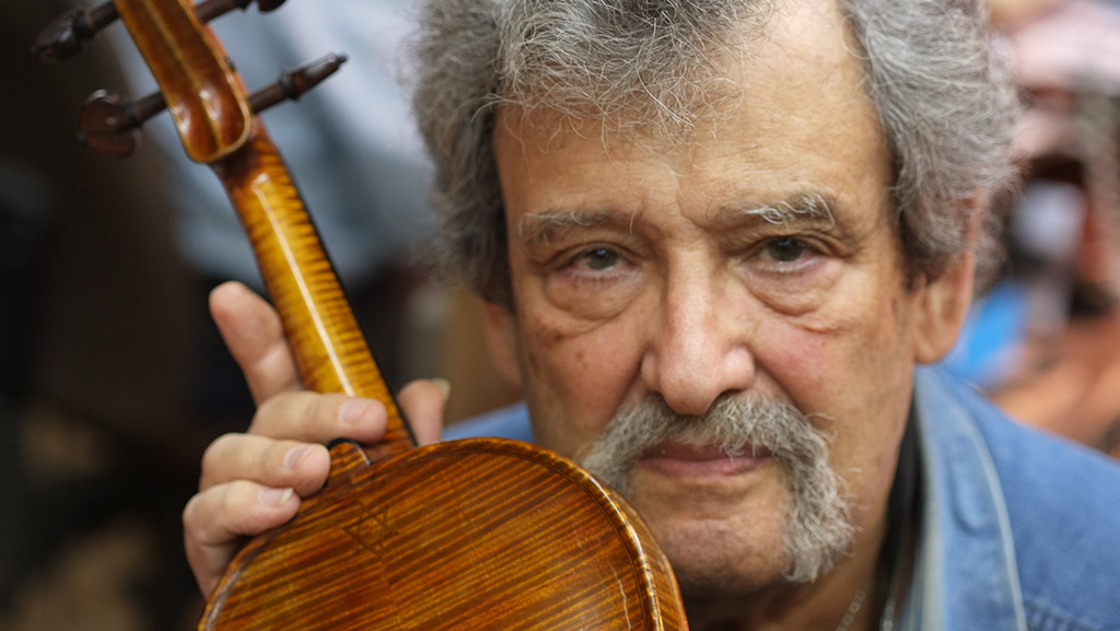 A close up of Amnon Weinstein holding a violin with the backside facing the camera