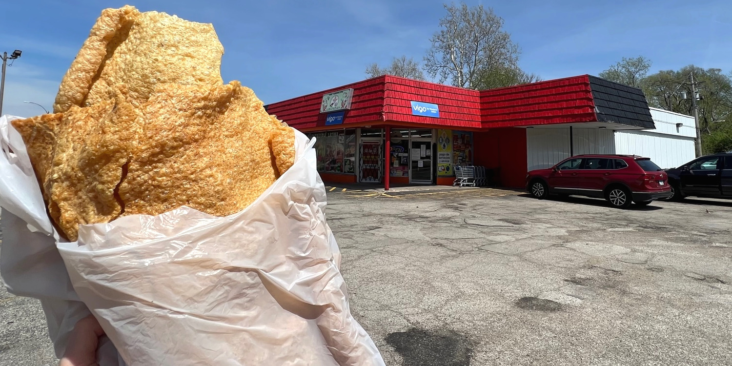 A plastic grocery bag with chicharrón in front of a red roofed grocery called Los Paisas. Photo by Alyssa Buckley.