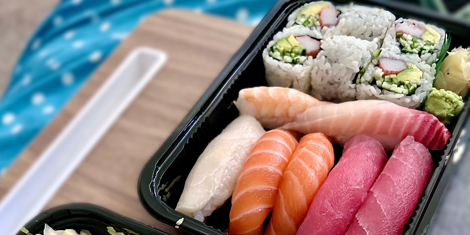 A cropped photo shows a black plastic takeout container full of sashmi, nigiri, and one sushi roll from Sushi Man in Champaign, Illinois as part of a list of sharable foods in Champaign-Urbana. Photo by Carolyn Cai.