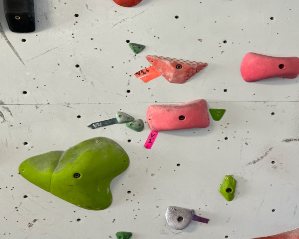 a white peg wall has rocks of various colors and shapes and tape in different colors to illustrate the climbing routes.