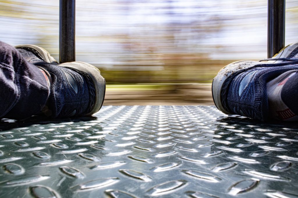a low angle photograph. the floor is in the foreground with legs extended in jeans and tennis shoes on each side. A blur motion is visible in the background
