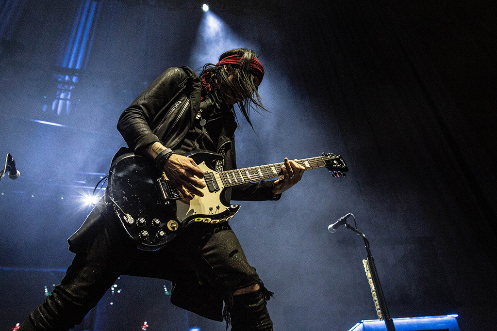 One of Alice Cooper's guitar players, performing onstage, dressed in black with a red bandana.