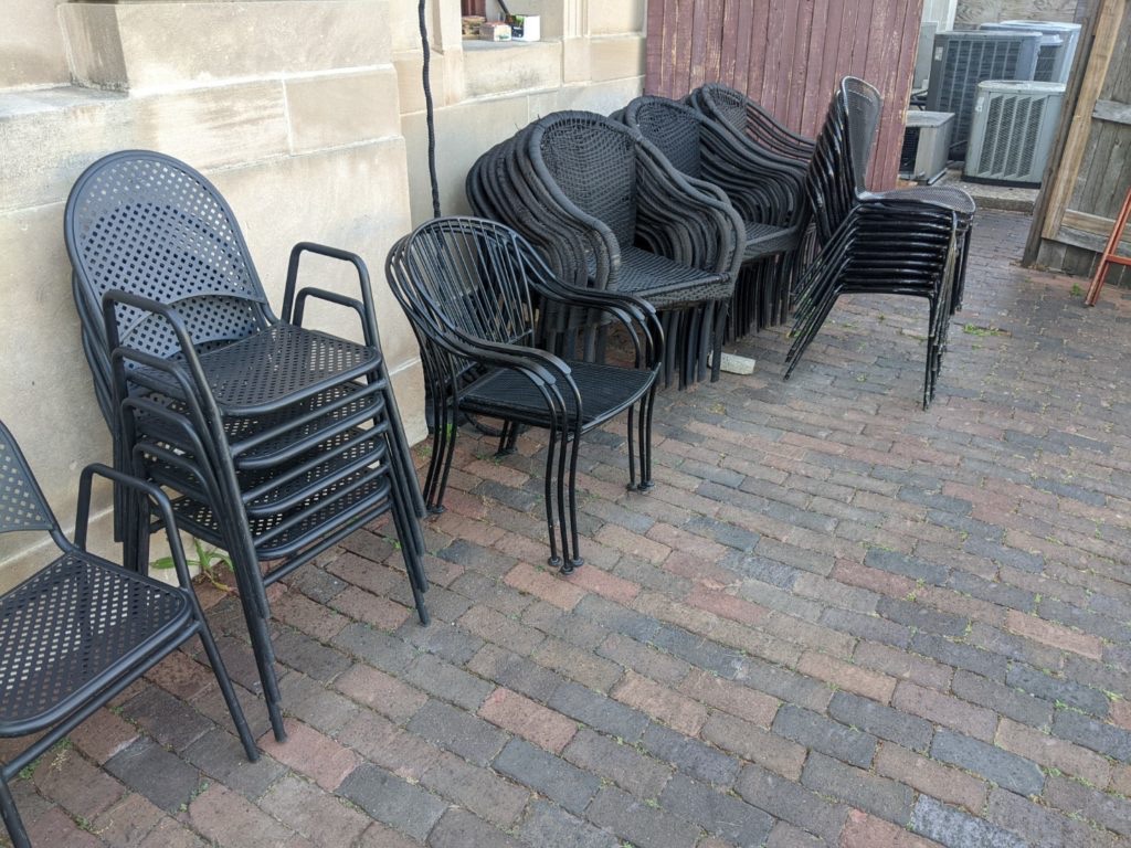 stacks of various black metal chairs sit unused against a white stone wall