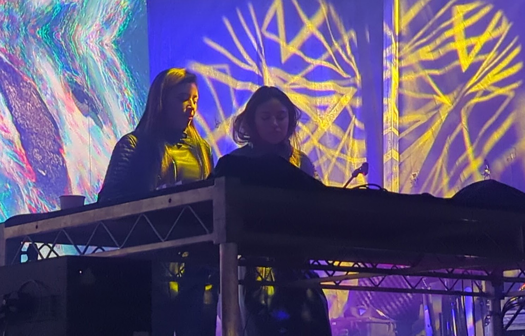 Two women behind a DJ table performing on stage.
