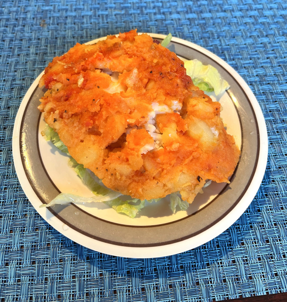Llapingachos at El Paraiso. A plate of seasoned mashed potatoes stuffed with cheese on a small white plate. The plate sits on a blue placemat.