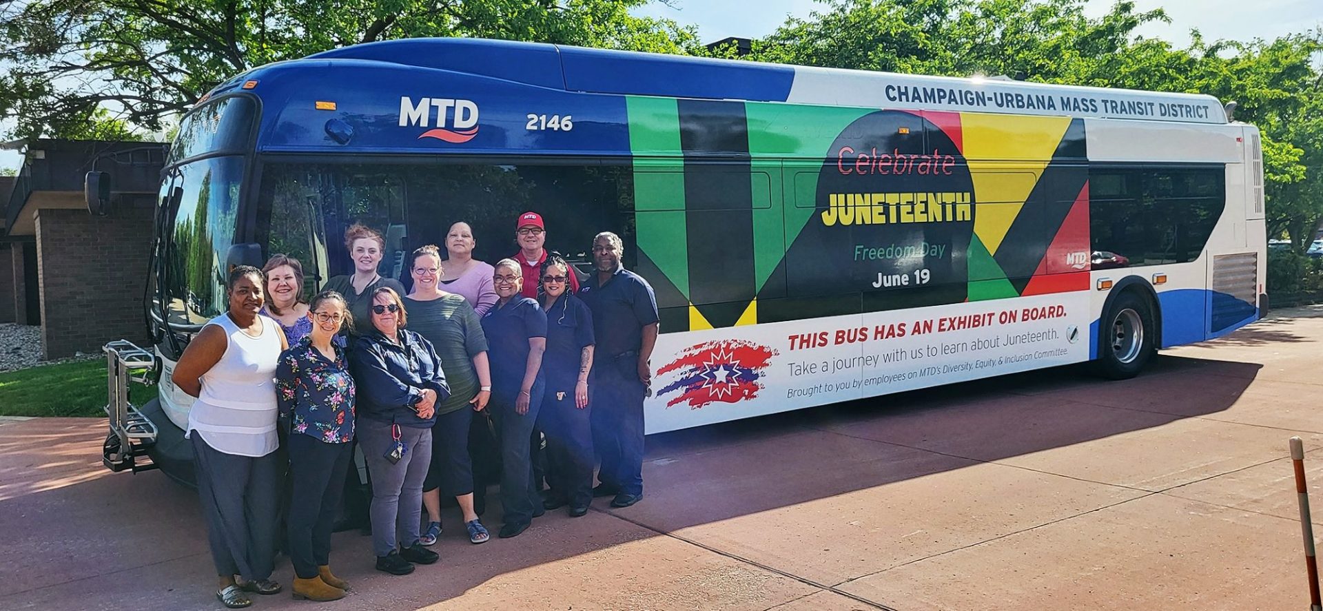 A group of people are standing in front of a city bus with the words Juneteenth in yellow, and accents of green, yellow, and red.