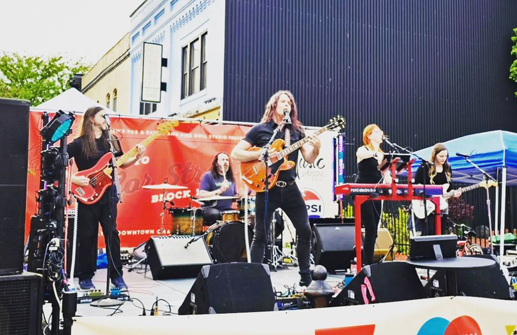 The five members of Modern Drugs playing on an outdoor stage as a part of Toast to Taylor Street in Downtown Champaign, IL.