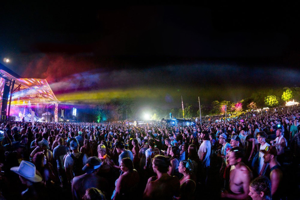 A photo of a crowded music festival at night. The stage is lit up and there are thousands of people in the audience