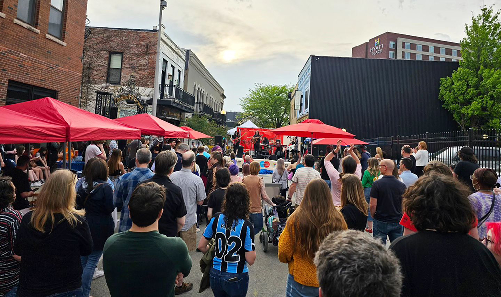 A crowded street festival with a band playing at the end of the street