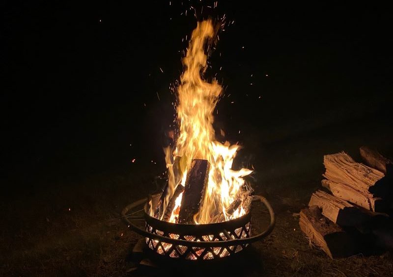 A campfire in a metal fire pit, with orange flames reaching a foot into the air.