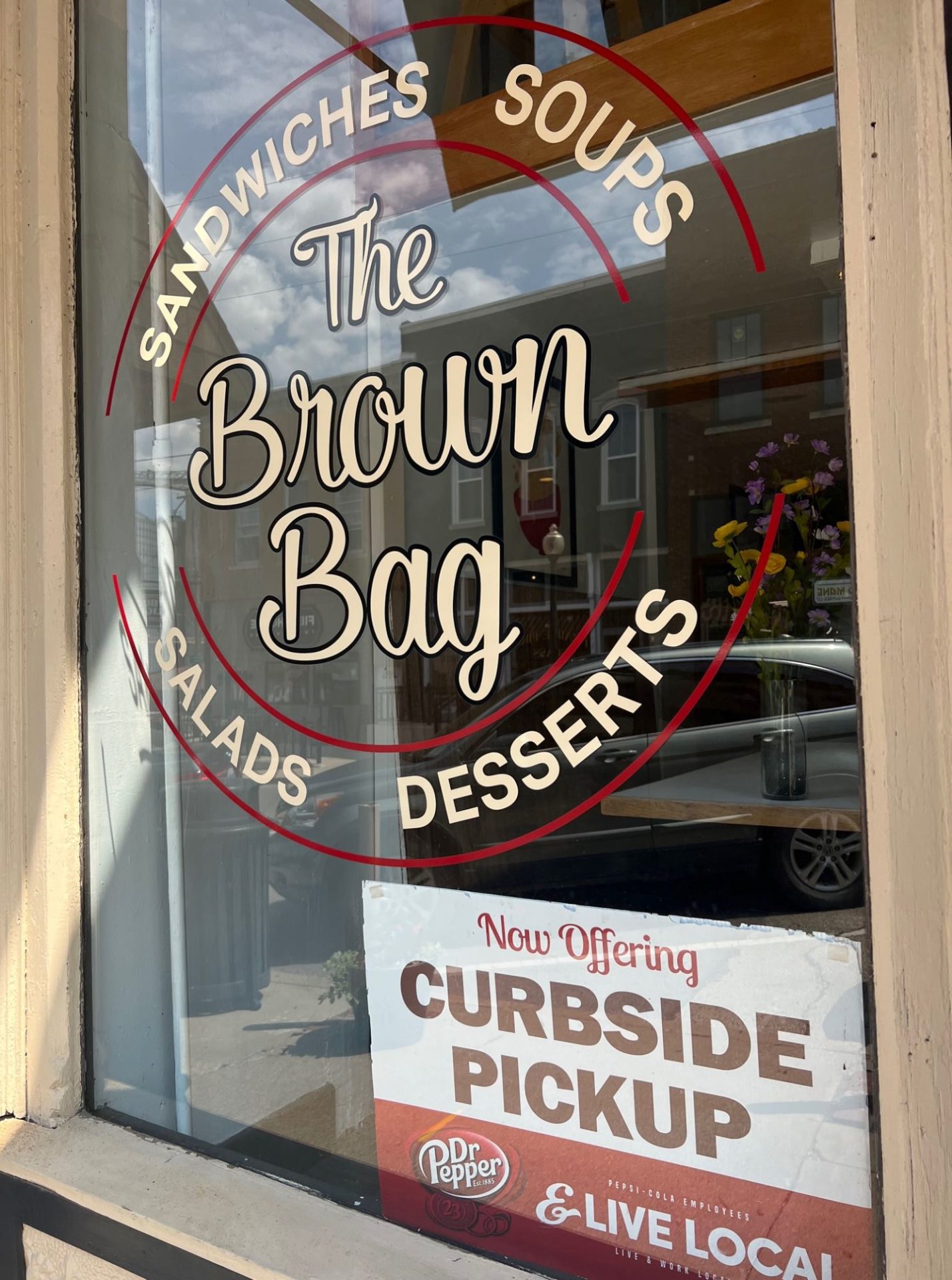 A window that has The Brown Bag painted on it in beige script. There are two red circles around the words.