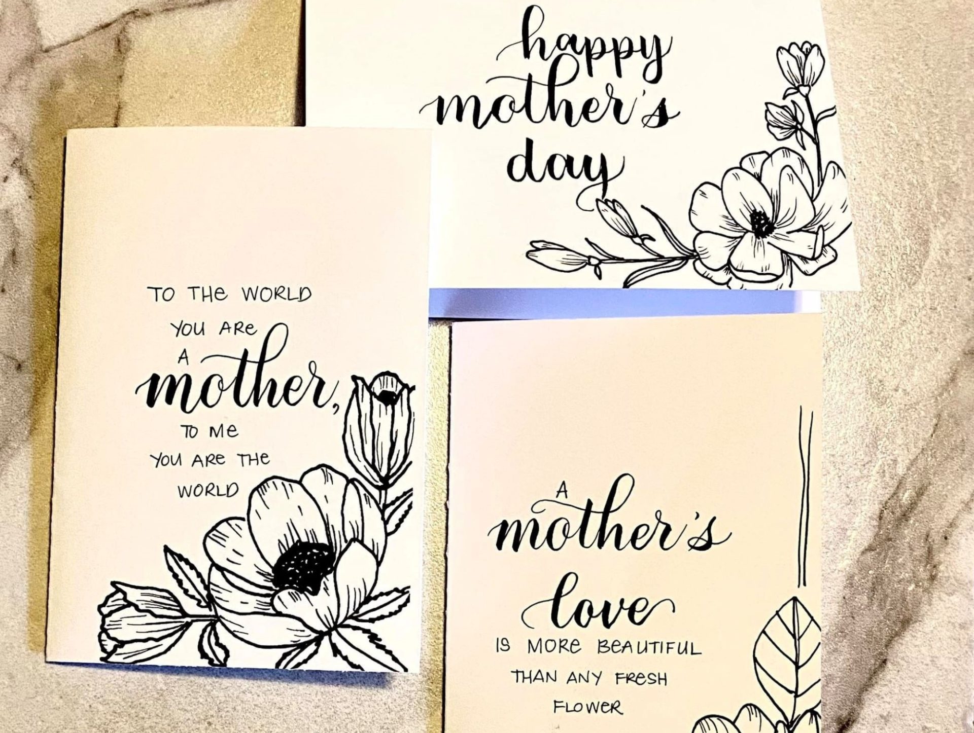 Three Mother's Day cards with black lettering and floral designs are sitting on a table.