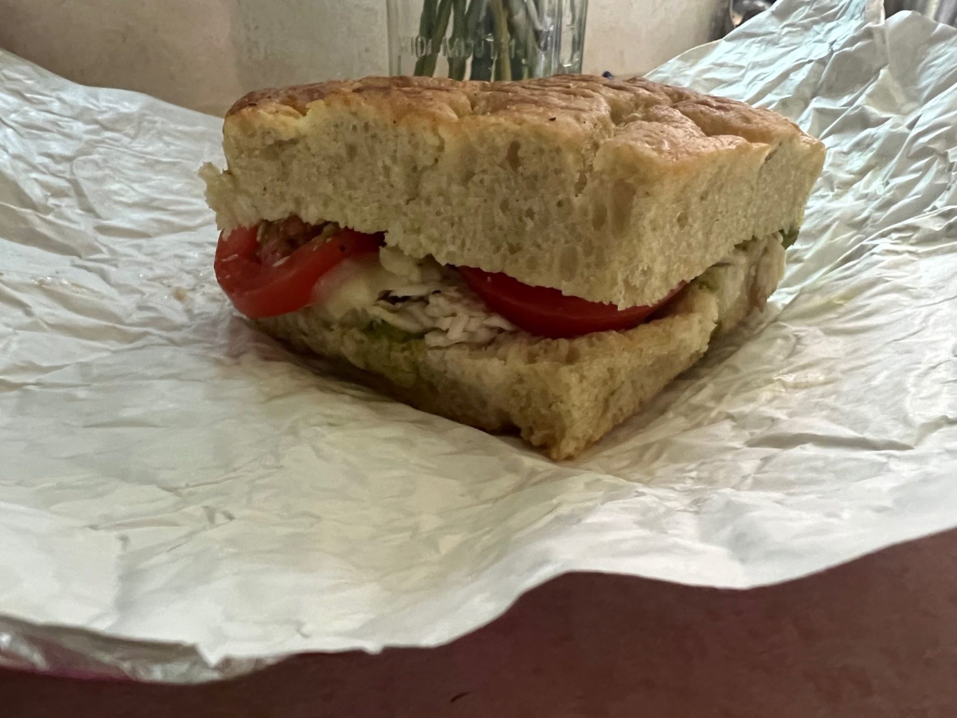 A sandwich with thick focaccia bread, turkey, and tomatoes is sitting on a white wrapper.
