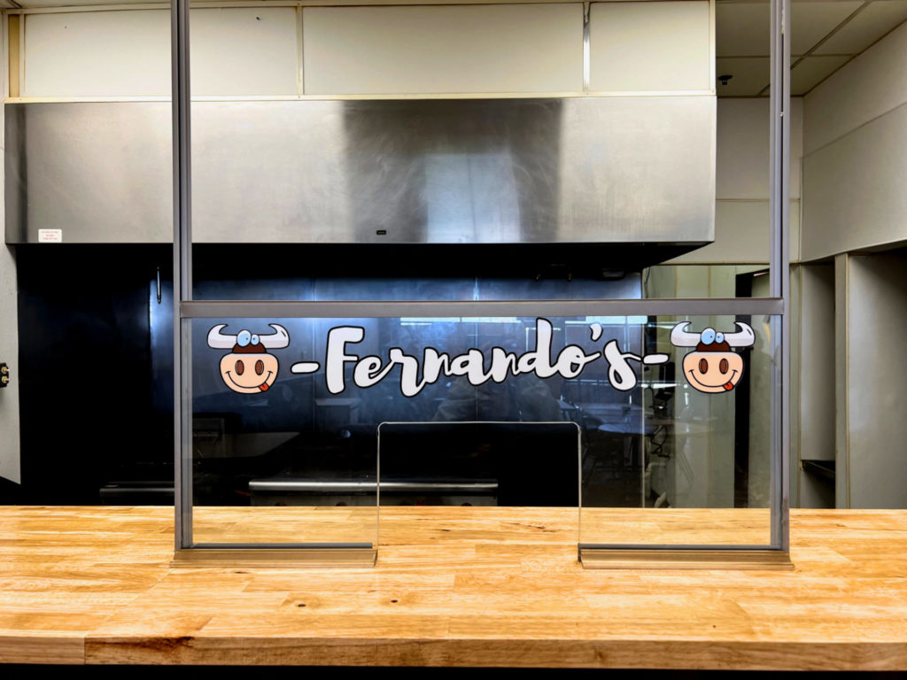 Inside the new Fernando's restaurant is a glass divider with the name of the restaurant and the cow logo on either side of the letters. The glass is on a light brown butcher block counter separating the dining room from the kitchen. Photo by Alyssa Buckley.
