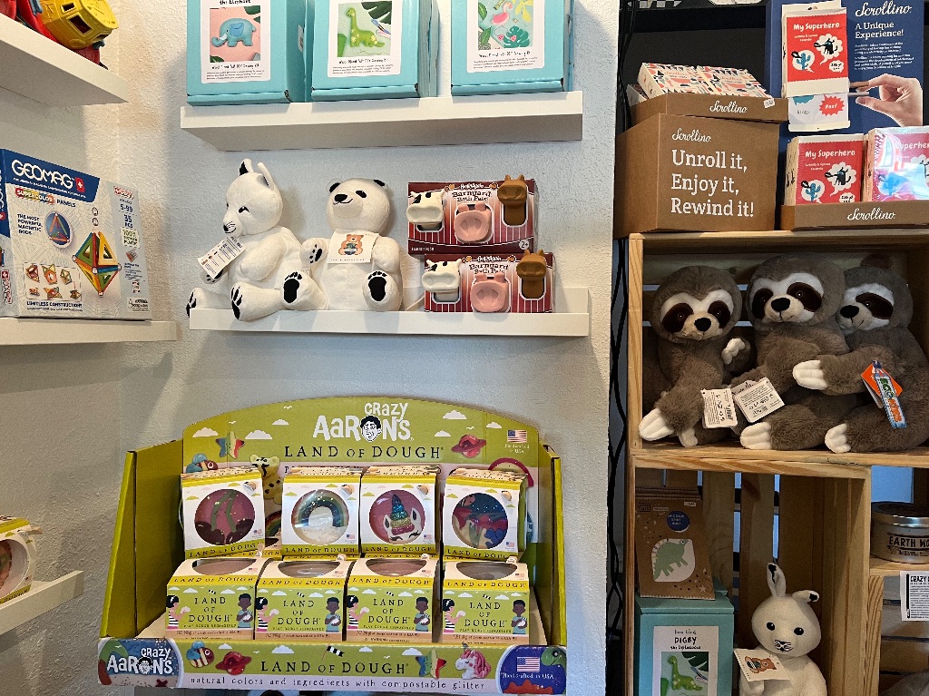 A wall of shelves full of toys including, sloth stuffed animals and colorful play dough