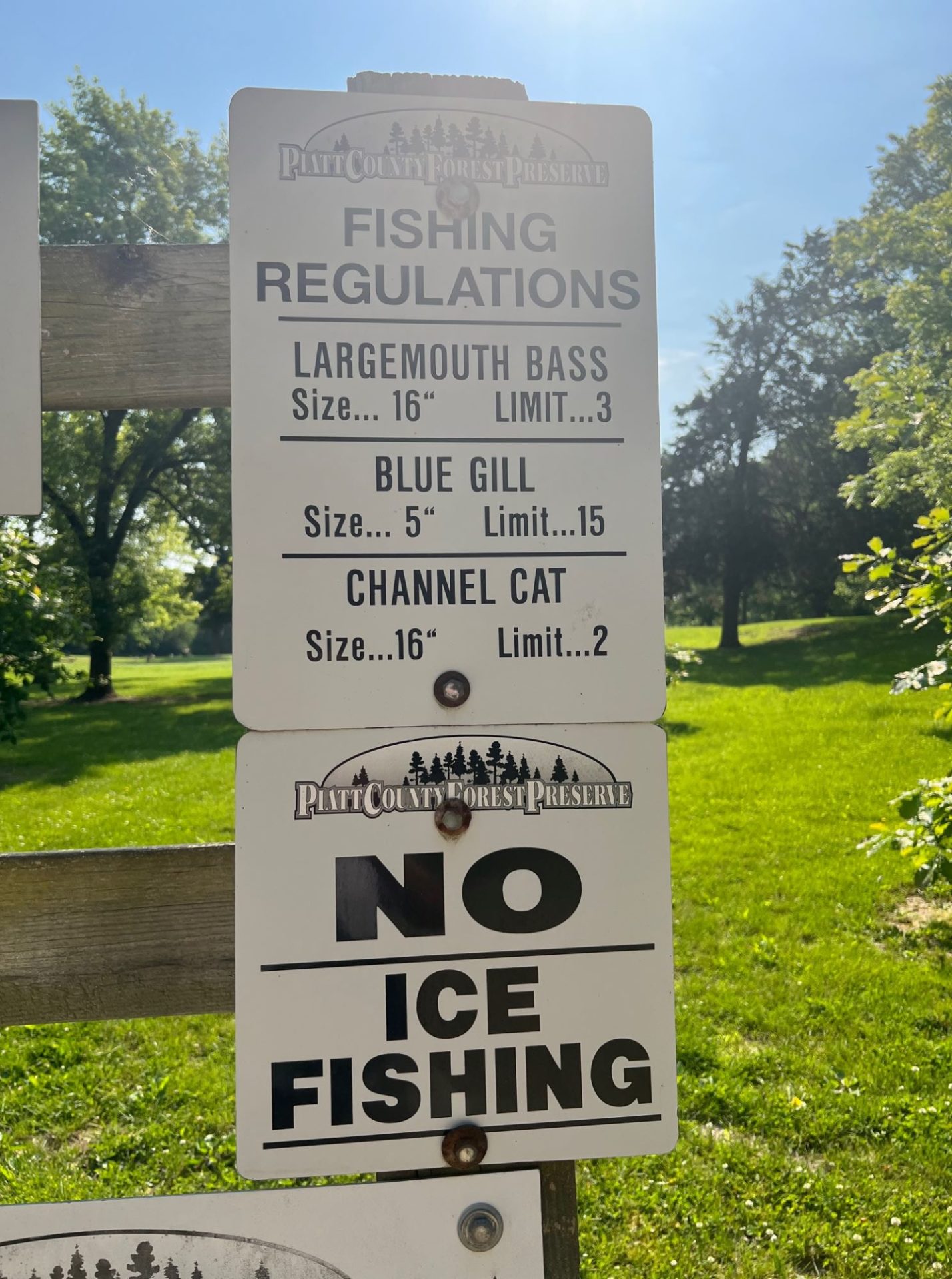 Two white signs with black lettering stacked on top of each other. The top sign lists fishing regulations. The bottom sign says NO ICE FISHING in black block letters.