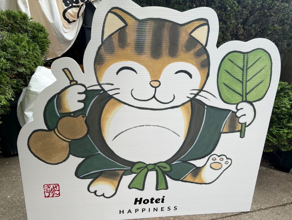 An illustrated cat wearing a green kimono and holidng a leaf in one hand.