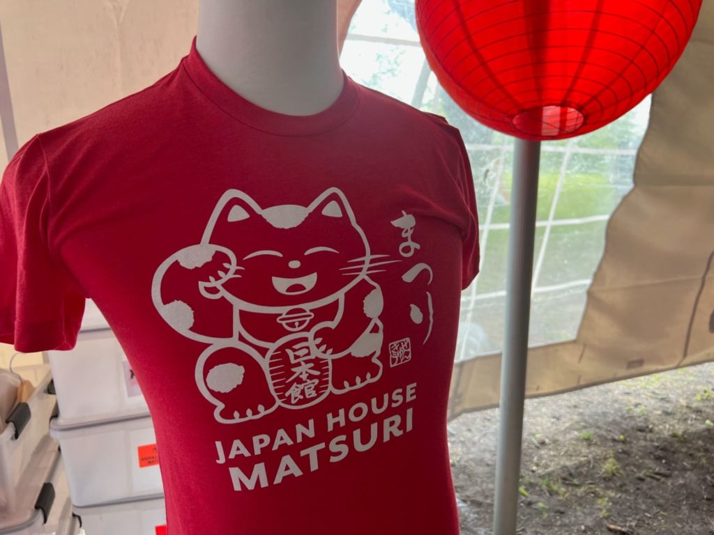 A mannequin bust with a red t-shirt covering it. The shirt has white lettering that says Japan House Matsuri, and there is a white outlined Japanese style cat. 