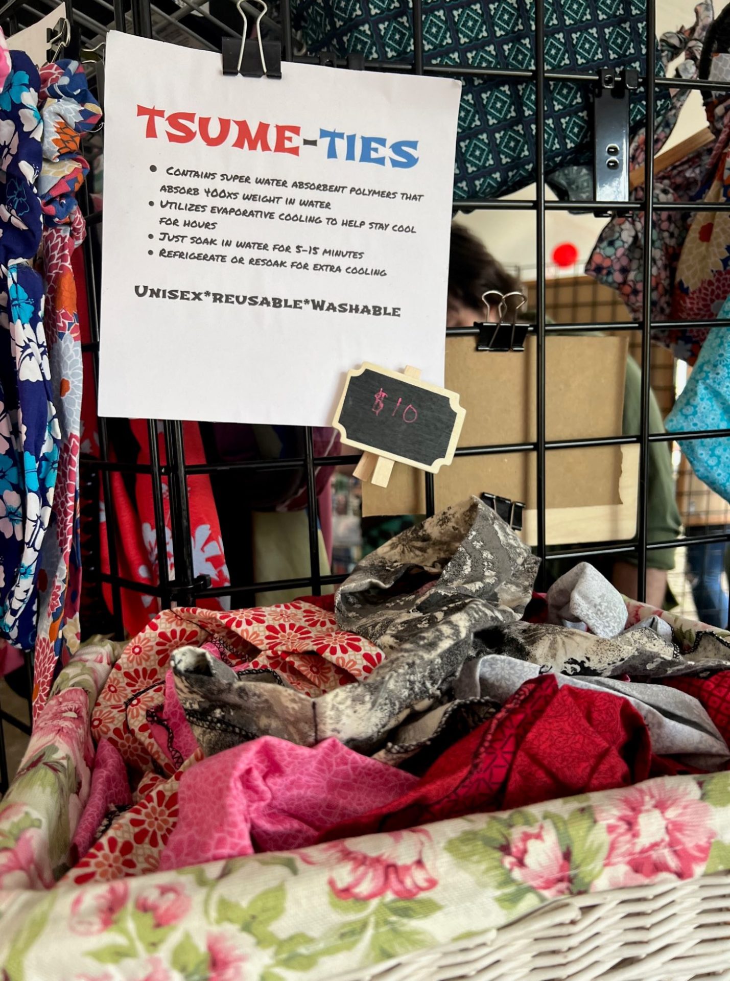 A basket of colorful patterned pieces of fabric sit on a shelf, below a white sheet of paper that says Tsume-Ties in red and blue lettering.