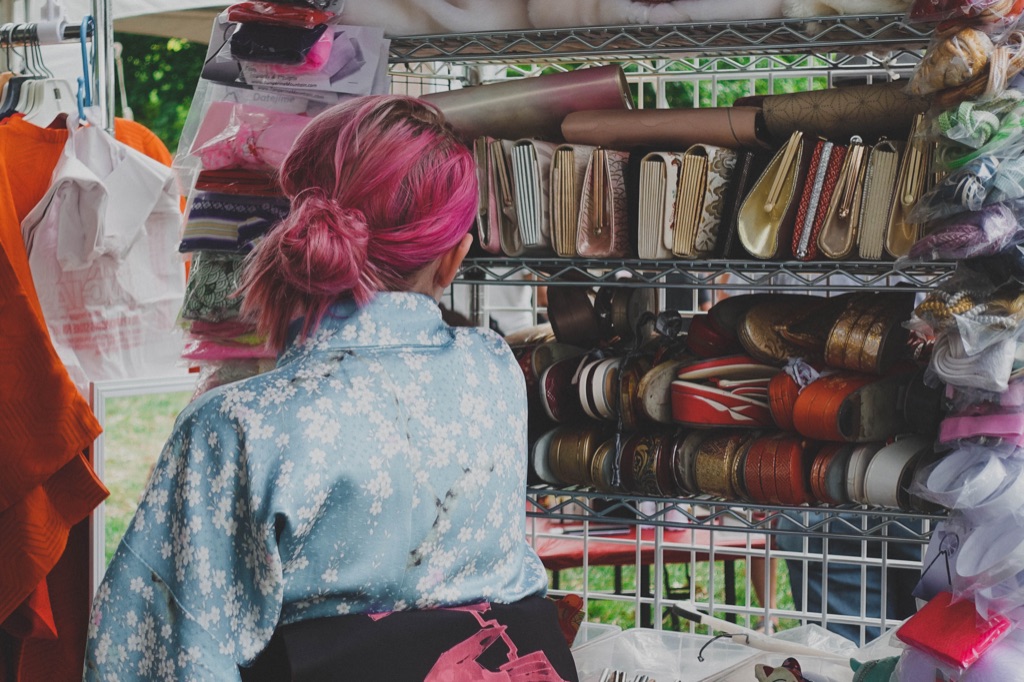 the back of a persons head with pink har tied back in a loose bun. They are wearing a sky blue kimono with small white flowers on it. They are looking at a shelf full of purses and slippers.