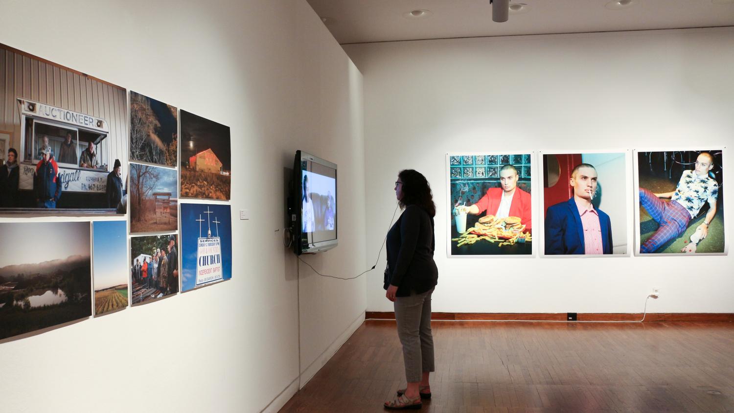 A woman stands in the art gallery at Krannert Art Museum, she is looking at a digital display while surrounded by paintings
