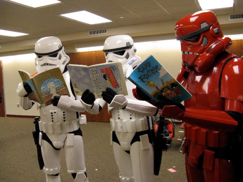two white storm troopers and one red storm trooper stand in a semi-circle reading children's books.