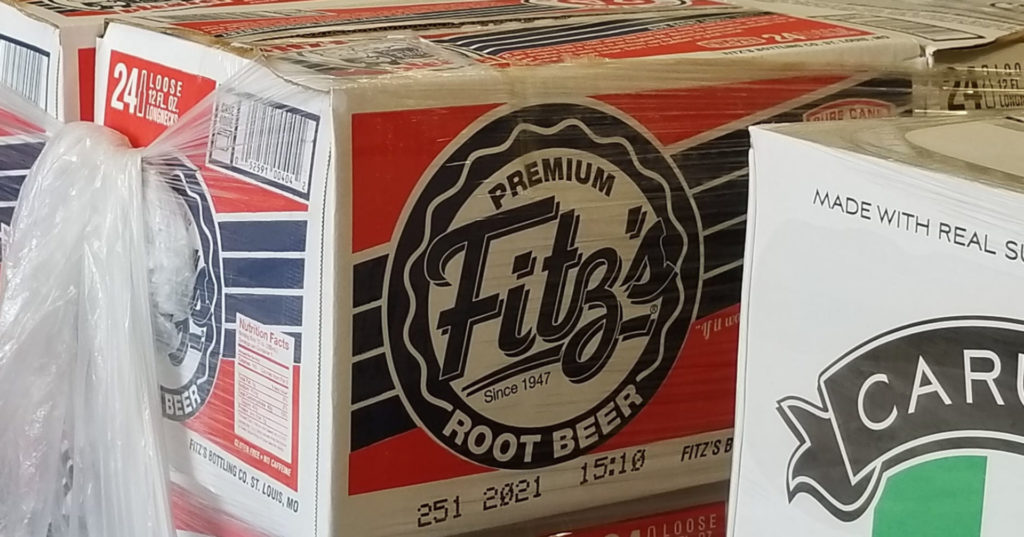 A box holding a case of Fitz's rootbeer is stacked on other boxes of soda. The box is red and white with blue text.