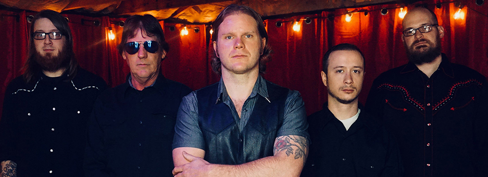5 members of Caleb Cook band in a dark room with a string of lights in front of a red curtain in the background