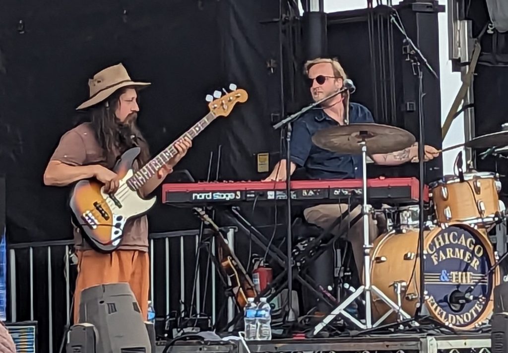 A bass player and a drummer performing on an outdoor stage.