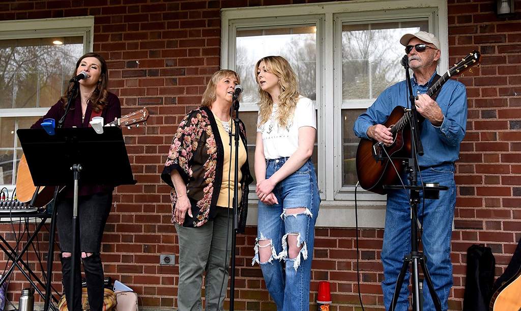 4 members of the Hood Family Band performing on the porch of a house.