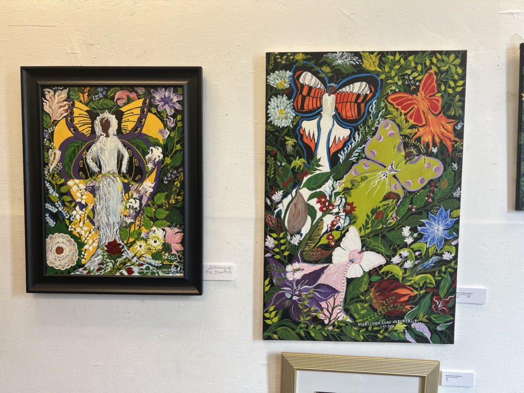 Two paintings by Marilyn Dean Cleveland. Both feature bright colors- primarily green with yellow and oranges. They resemble gardens. The painting on the left has a black woman in the center surrounded by the plants and flowers. The painting on the right has large butterflies as a focal point.
