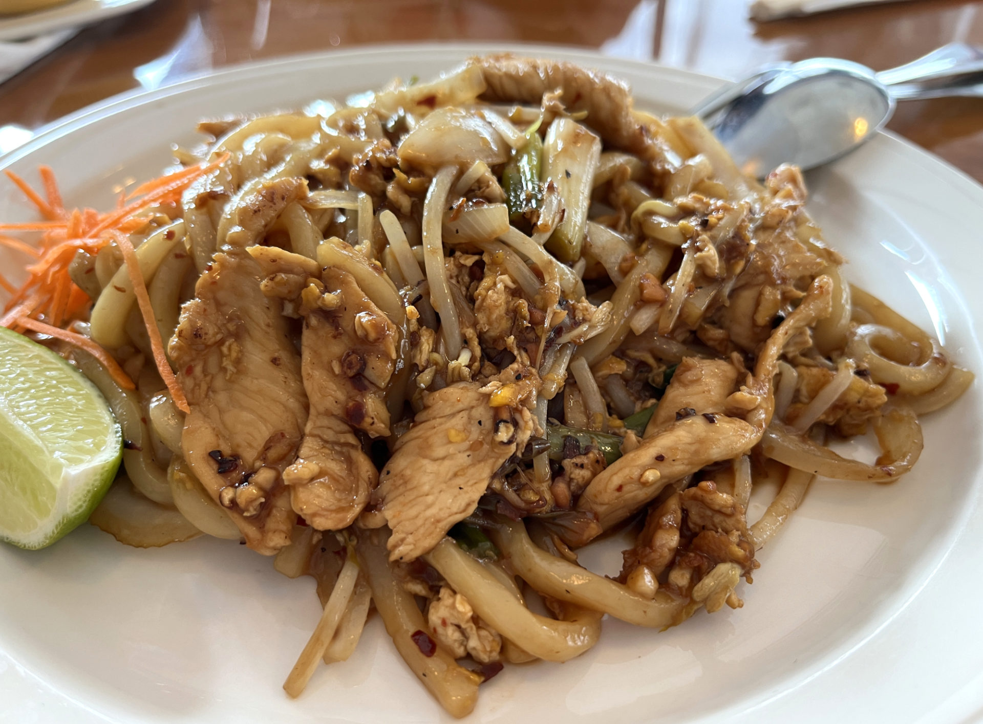 Chicken Pad Thai at Thara Thai. A white plate holds a heaping pile of noodles and chicken, a slice of lime and some carrot shavings.