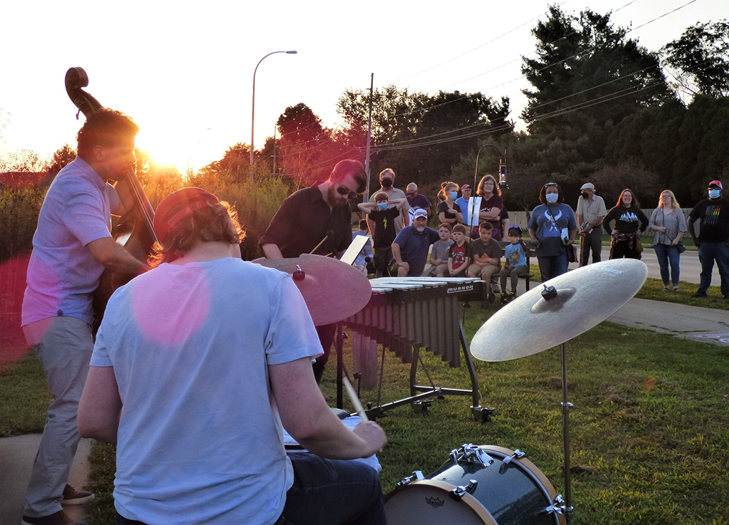 3 Members of the Matthew Miller Trio playing an outdoor concert. The photo is taken from behind the drummer and you can see the audience about 20 feet in the distance.